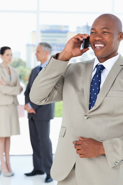 Jonge manager die op de telefoon lachen terwijl zijn team op de achtergrond is