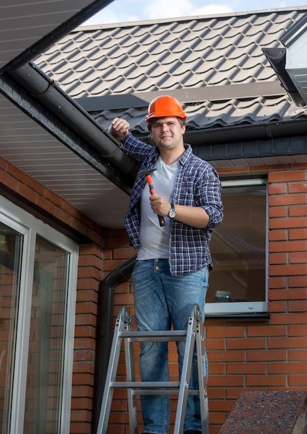 Jonge mannelijke arbeider die zich op stapladder voor huis bevindt