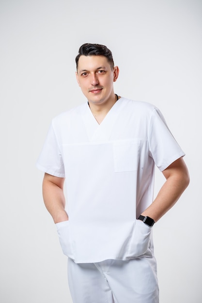 Jonge mannelijke arts in een wit chirurgisch pak. Geïsoleerd op een witte achtergrond