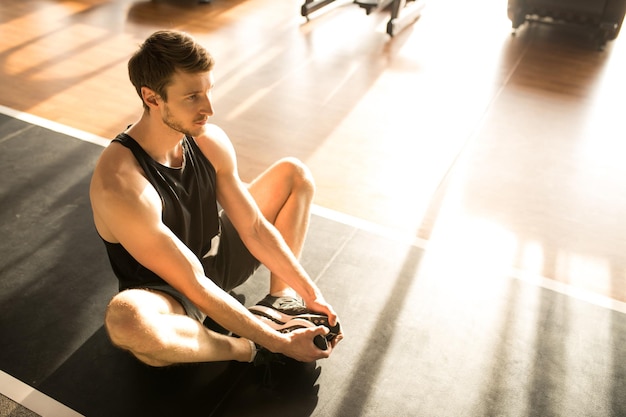 Jonge mannelijke atleet die er gefocust uitziet terwijl hij op de grond zit en oefeningen doet in de gezondheidsclub