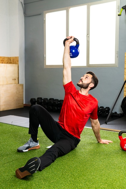 Jonge mannelijke atleet die zware kettlebell op betonnen vloer grijpt tijdens gewichtheffen in de sportschool