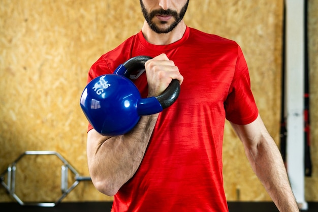 Jonge mannelijke atleet die zware kettlebell op betonnen vloer grijpt tijdens gewichtheffen in de sportschool