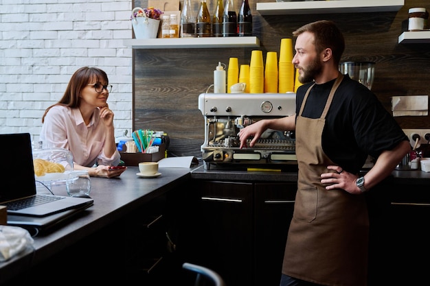 Jonge mannelijke barista die praat met een vrouwelijke klant in een koffiewinkel