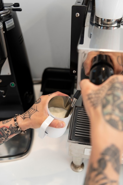 Jonge mannelijke barista met tatoeages die de koffiemachine gebruiken op het werk