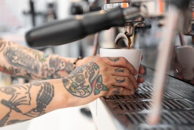 Jonge mannelijke barista met tatoeages die de koffiemachine gebruiken op het werk