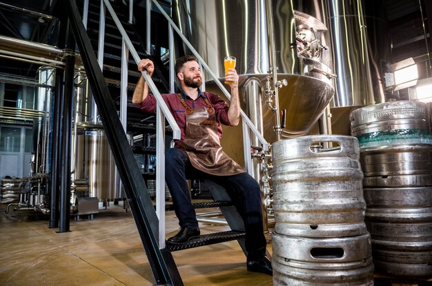 Jonge mannelijke brouwer in leren schort bij moderne brouwerijfabriek