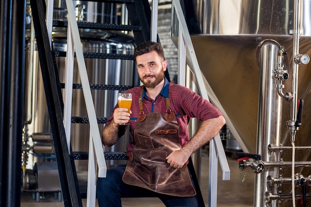 Jonge mannelijke brouwer in leren schort bij moderne brouwerijfabriek