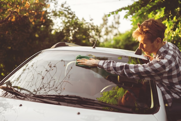 Jonge mannelijke chauffeur veegt zijn auto buiten af op zomerdagen