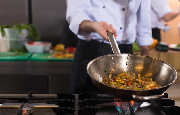 Jonge mannelijke chef-kok die groenten in wok omdraait bij commerciële keuken