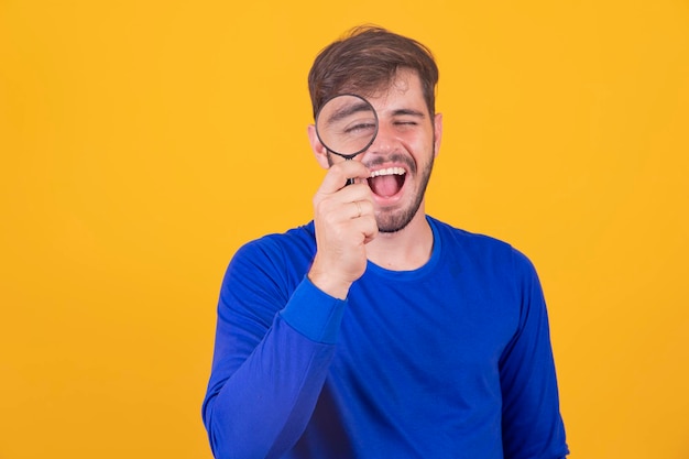 Jonge mannelijke detective die vergrootglas met het rechteroog vasthoudt terwijl hij geïsoleerd voor de camera staat