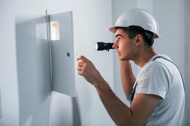 Jonge mannelijke elektricien in witte helm werkt binnenshuis in de kamer