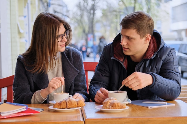 Jonge mannelijke en vrouwelijke vriendenstudenten die in openluchtkoffie zitten