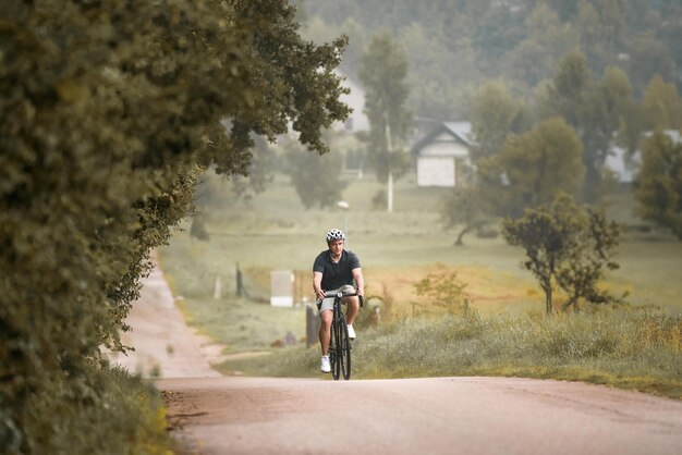 Jonge mannelijke fietser die een actieve levensstijl omarmt Een vooraanzicht van een fietser die op zijn grindfiets rijdt op het platteland