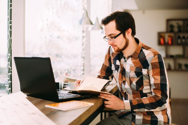 Jonge mannelijke freelancer die laptop met behulp van terwijl het zitten in koffiewinkel