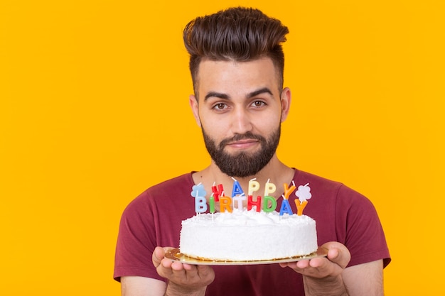 Jonge mannelijke hipster met een baard met een taart met de inscriptie gelukkige verjaardag gefeliciteerd
