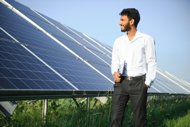 Jonge mannelijke ingenieur met tablet in de hand die bij zonnepanelen staat