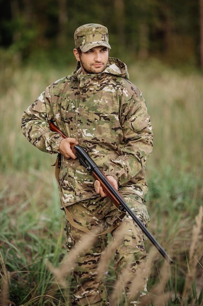 Jonge mannelijke jager in camouflagekleding klaar om te jagen met jachtgeweer