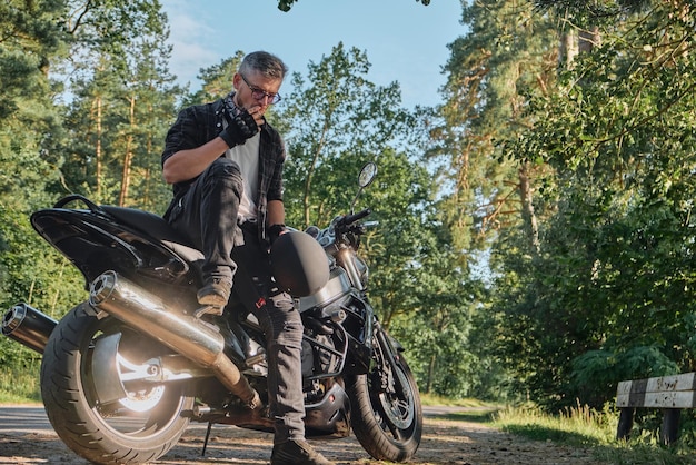 Jonge mannelijke motorrijder reist alleen op een motorfiets, stopte en rookte aan de kant van een bosweg