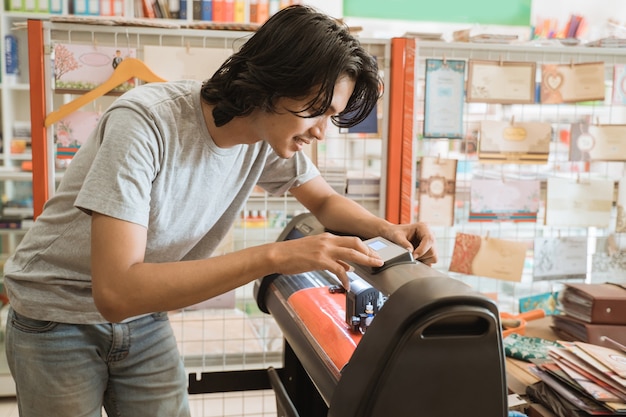 Jonge mannelijke ondernemer Stickerpapier maken door machine die in een kantoorboekhandel werkt