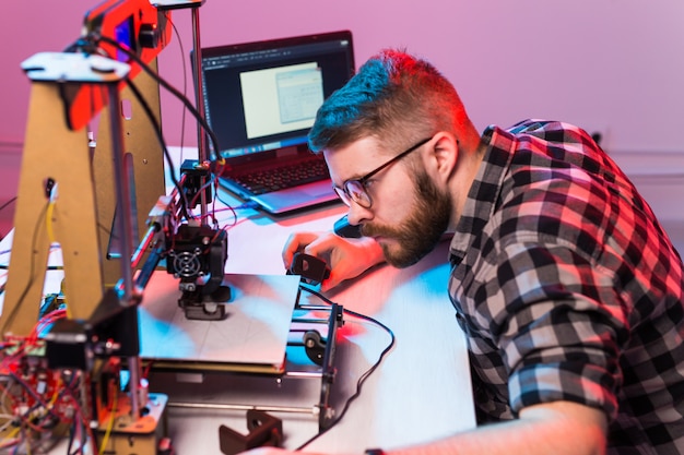 Jonge mannelijke ontwerperingenieur die een printer in het laboratorium gebruikt en een productprototype bestudeert