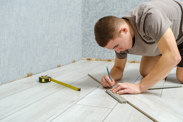 Jonge mannelijke reparateur markeert een houten paneel met een potlood en een liniaal voordat hij wordt gesneden. Laminaatvloer, kopie ruimte.