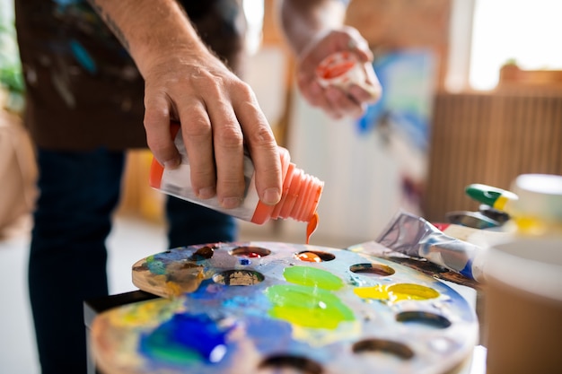 Jonge mannelijke schilder gouache van oranje kleur toe te voegen aan palet voordat hij verven mengt tijdens het werk in de studio