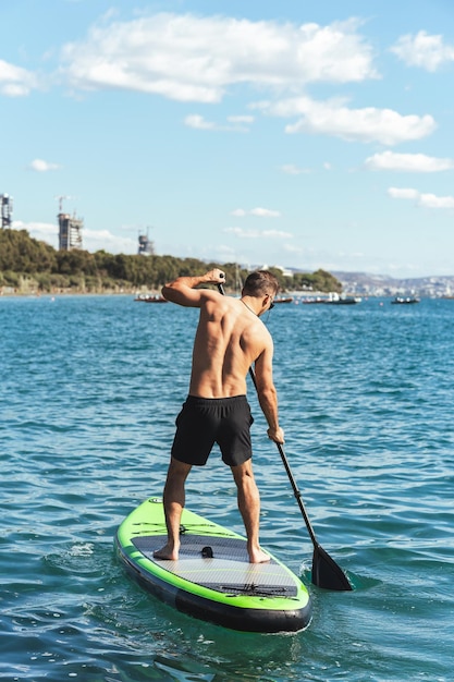 Jonge mannelijke surfer die stand-up paddleboard berijdt in oceaan