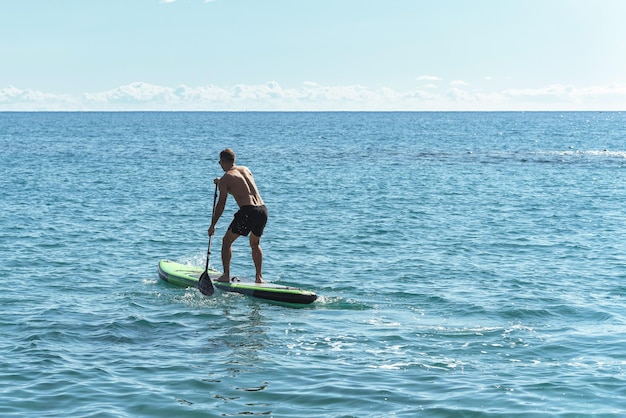 Jonge mannelijke surfer die stand-up paddleboard berijdt in oceaan