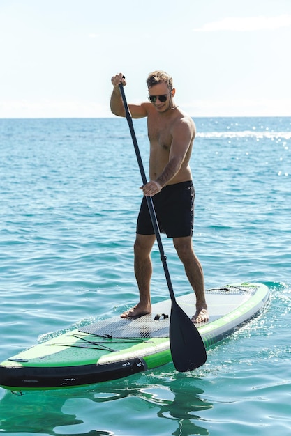 Jonge mannelijke surfer die stand-up paddleboard berijdt in oceaan