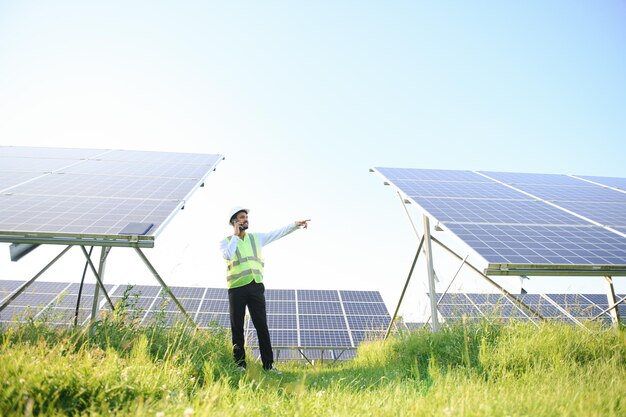 Jonge mannelijke technicus die groene vesten en helm draagt en aan de telefoon praat over het onderhoud en de installatie van de zonnepanelen die in veldtechnologie in de landbouw staan