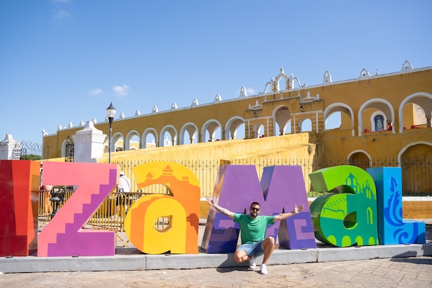 Foto jonge mannelijke toerist die een foto maakt met de kleurrijke letters izamal bij de ingang van het klooster van san antonio mexico