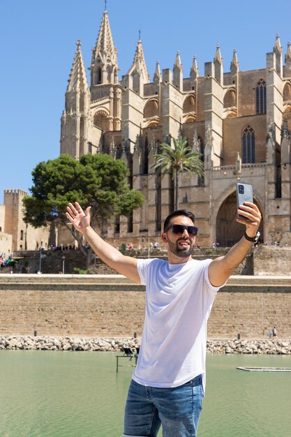 Jonge mannelijke toerist die zichzelf fotografeert voor de kathedraal van Palma de Mallorca op een zonnige dag in Spanje