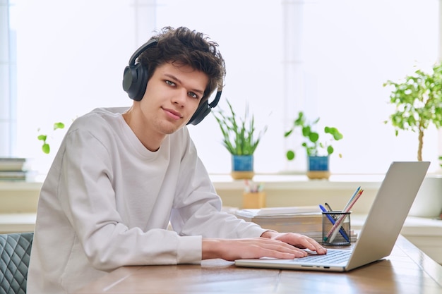Jonge mannelijke universiteitsstudent zit aan een bureau met een laptop en kijkt naar de camera
