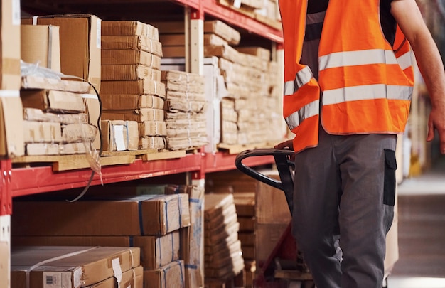 Jonge mannelijke werknemer in uniform is in het magazijn en duwt pallettruck.