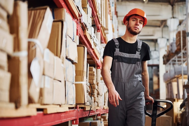 Jonge mannelijke werknemer in uniform is in het magazijn en duwt pallettruck.