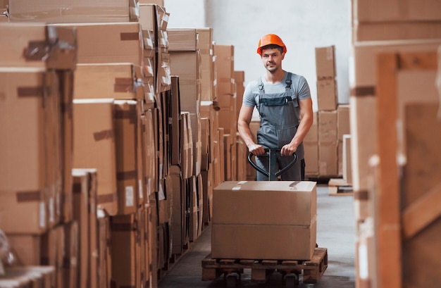 Jonge mannelijke werknemer in uniform is in het magazijn met pallettruck.