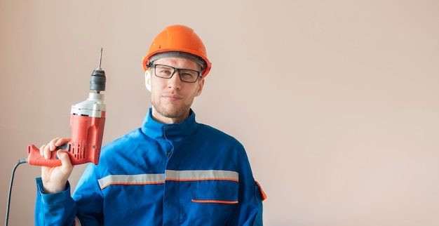 Jonge mannelijke werknemer in uniform met de boor van het elektrische gereedschap