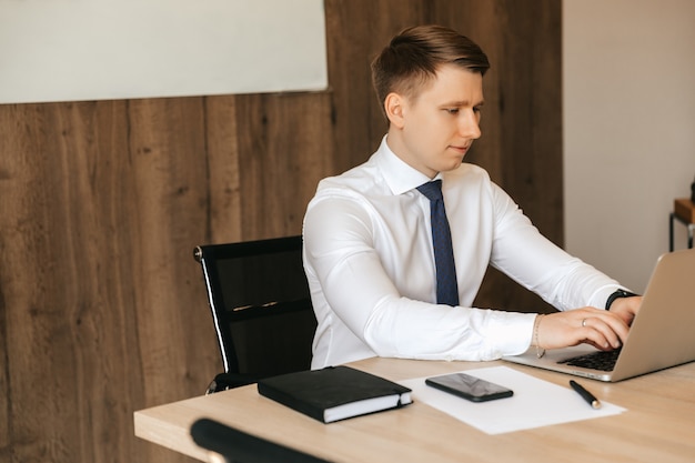 Jonge mannelijke zakenman die aan laptop in bureau werkt.