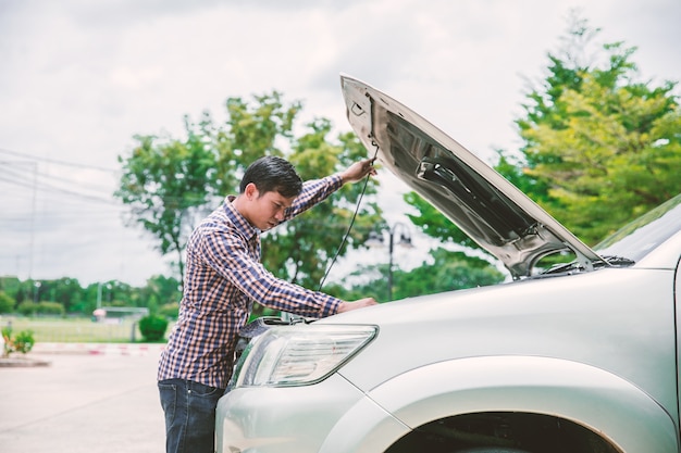 Jonge mannen dichtbij zijn gebroken auto die op hulp wachten.