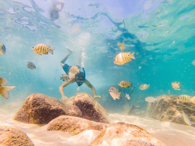 Jonge mannen die aan het snorkelen zijn en de onderwaterlandschapsachtergrond van het koraalrif in de diepblauwe oceaan verkennen met kleurrijke vissen en zeeleven