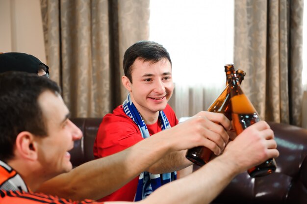 Jonge mannen drinken bier, eten chips en rooten voor voetbal