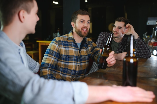 Jonge mannen in vrijetijdskleding praten, lachen en drinken terwijl ze aan de toog in de kroeg zitten