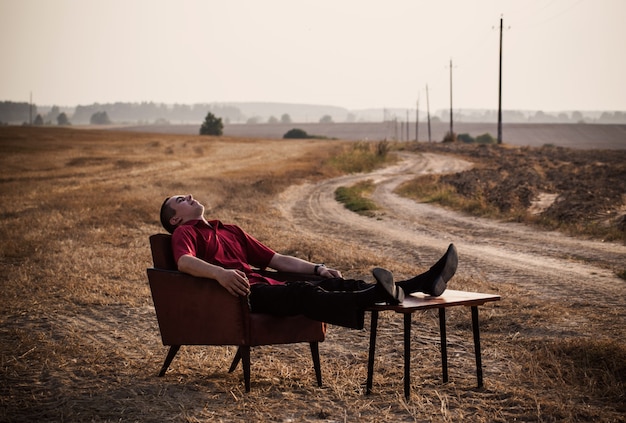 Foto jonge mannen op oude fauteuil in zomer veld