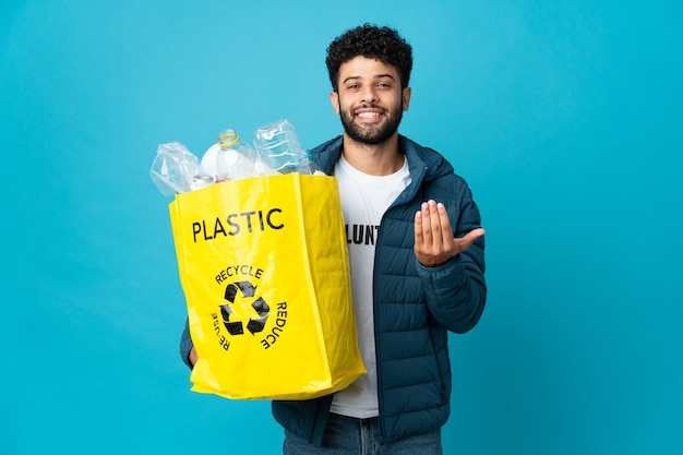 Jonge Marokkaanse man die een zak vol plastic flessen vasthoudt om te recyclen en uitnodigt om met de hand te komen. Blij dat je gekomen bent