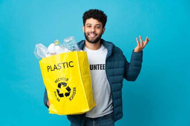 Jonge Marokkaanse man die een zak vol plastic flessen vasthoudt om te recyclen, zijn handen opzij om uit te nodigen om te komen