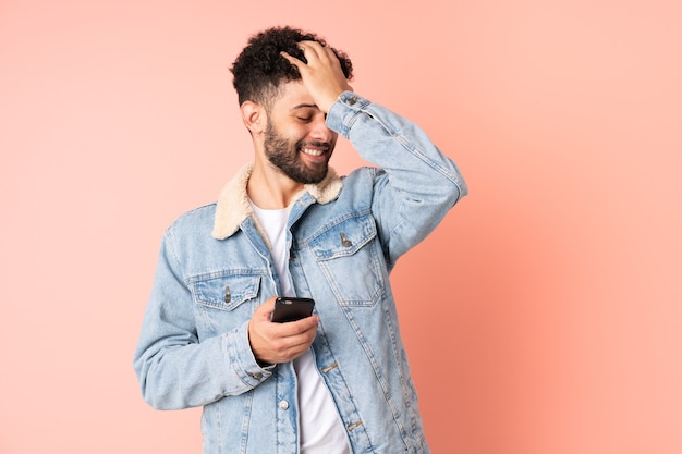 Jonge Marokkaanse man met behulp van mobiele telefoon geïsoleerd op roze muur heeft iets gerealiseerd en de oplossing voornemens