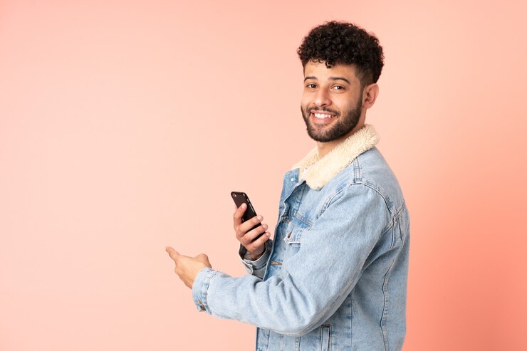 Foto jonge marokkaanse man met behulp van mobiele telefoon geïsoleerd op roze terug te wijzen