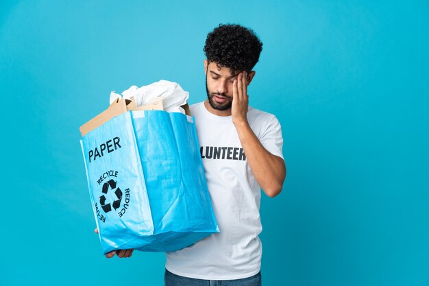 Jonge Marokkaanse man met een recyclingzak vol papier om te recyclen over geïsoleerde met hoofdpijn