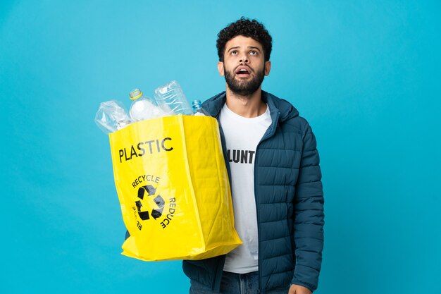 Jonge Marokkaanse man met een zak vol plastic flessen om te recyclen, opkijkend en met een verbaasde uitdrukking