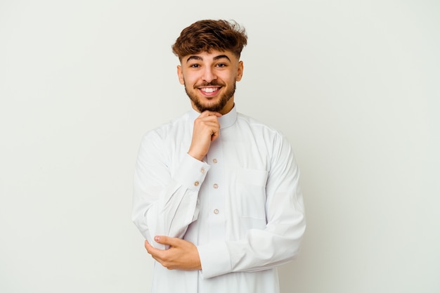 Jonge Marokkaanse man met typische Arabische kleding geïsoleerd op wit glimlachend gelukkig en zelfverzekerd, kin met hand aanraken.